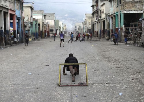 A man does push-ups while guarding a goal post as he and others play soccer on a street during an anti-government protest in Port-au-Prince